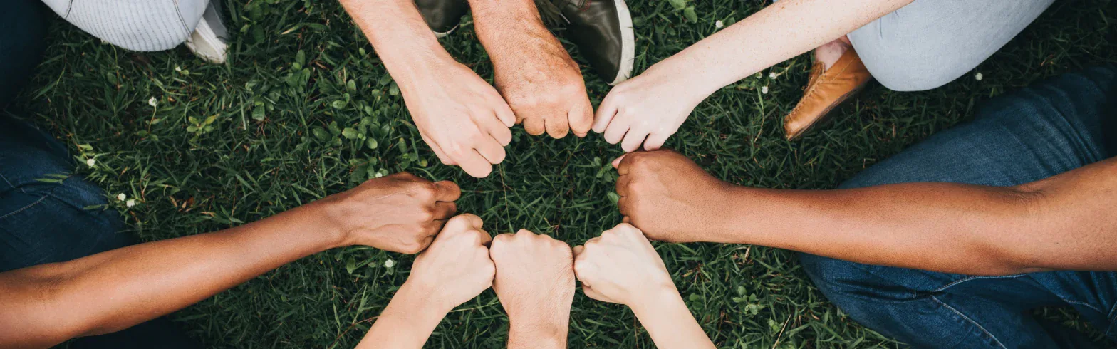 People standing in a circle with their fists joined over grass