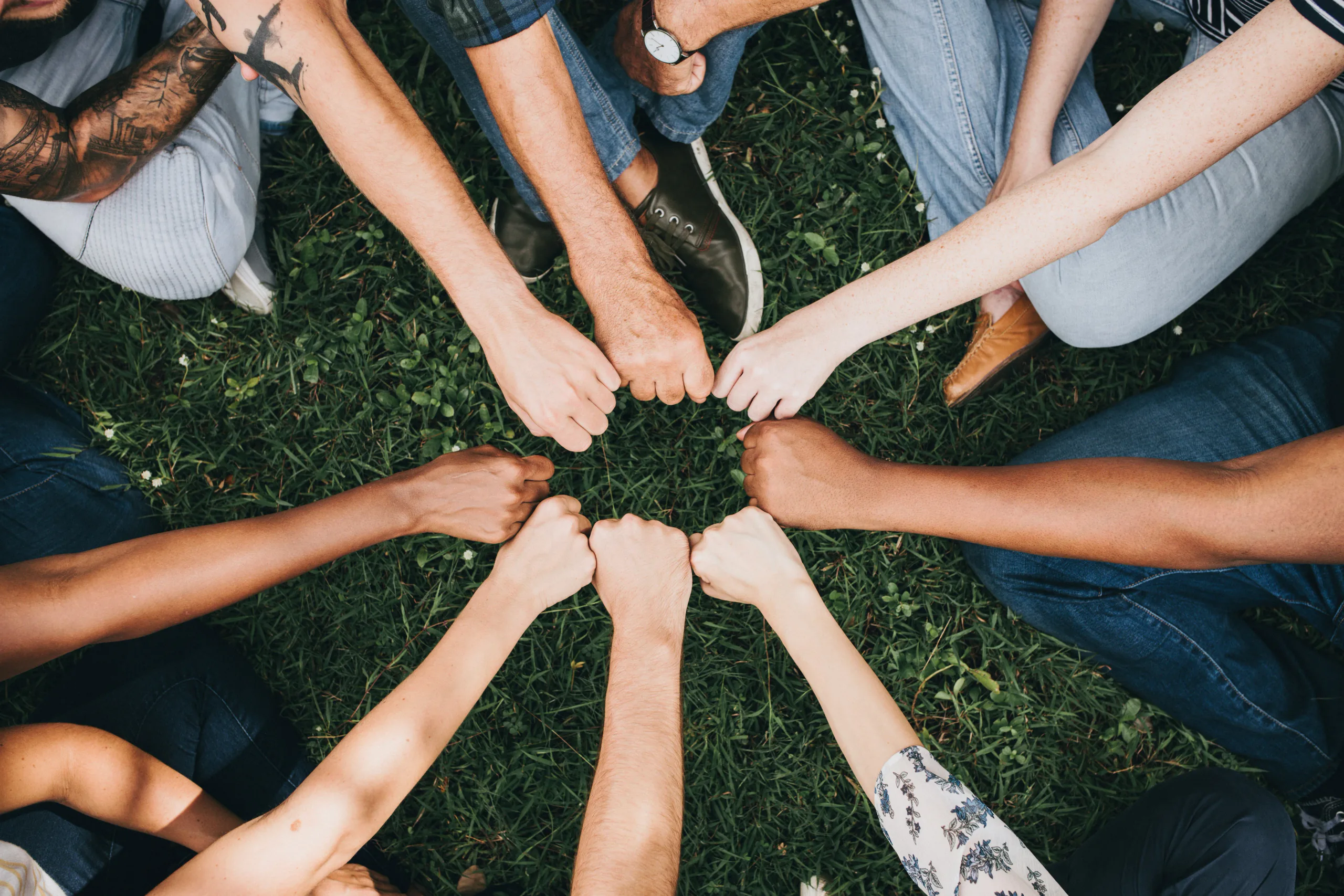 People standing in a circle with their fists joined over grass